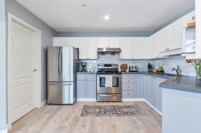 Kitchen featuring under cabinet range hood, light wood-style flooring, appliances with stainless steel finishes, white cabinets, and a sink | Image 14