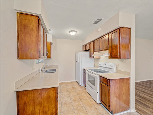 Kitchen with white appliances, a sink, under cabinet range hood, brown cabinetry, and light countertops | Image 9