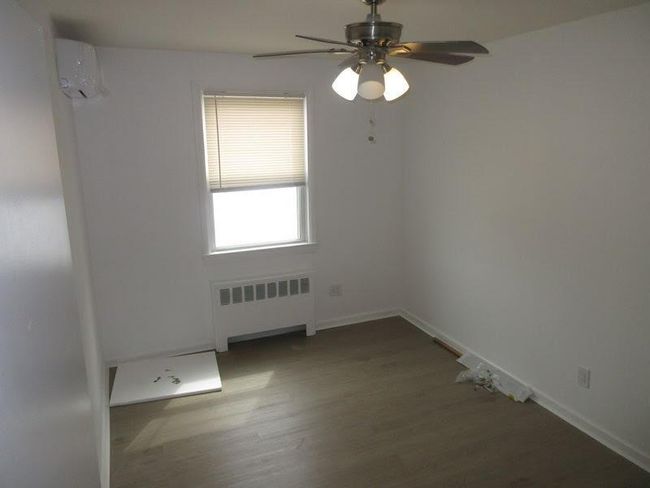 Unfurnished room with radiator heating unit, a ceiling fan, wood finished floors, and a wall mounted AC | Image 10