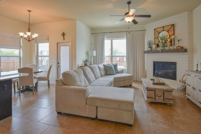 Tiled living room with ceiling fan with notable chandelier and a large fireplace | Image 8