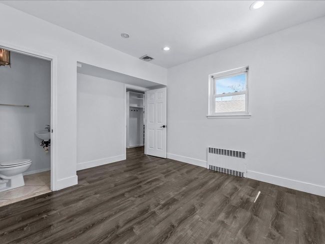 Unfurnished bedroom with radiator heating unit, baseboards, wood finished floors, recessed lighting, and ensuite bath | Image 11