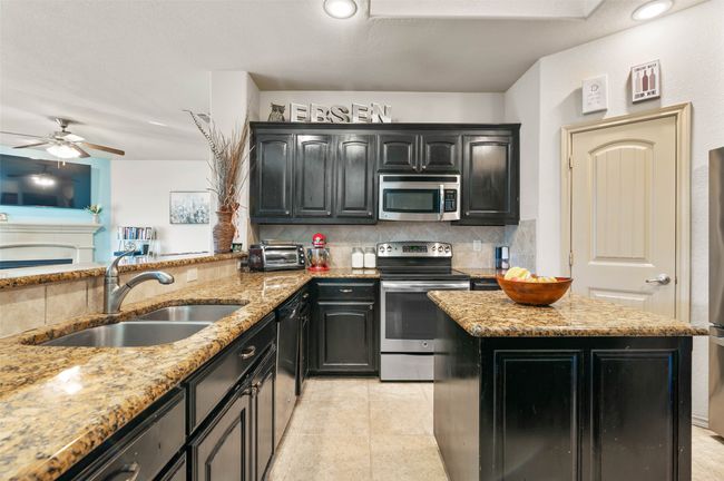 Kitchen featuring appliances with stainless steel finishes, backsplash, a sink, and light stone countertops | Image 13