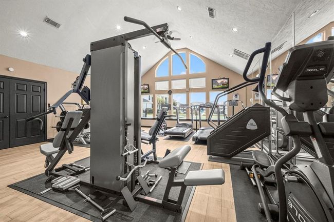 This is a spacious fitness center, with high ceilings, large windows for natural light, and a variety of exercise equipment. It features wood flooring and a neutral color scheme. | Image 31