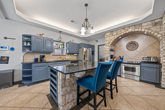 Kitchen with blue cabinets, stainless steel appliances, open shelves, tasteful backsplash, and a raised ceiling | Image 10