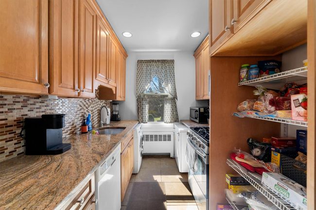 Kitchen with a sink, radiator, backsplash, light stone countertops, and appliances with stainless steel finishes | Image 13