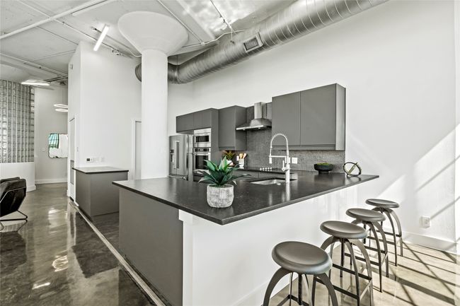 Kitchen with gray cabinets, appliances with stainless steel finishes, dark countertops, a kitchen bar, and wall chimney exhaust hood | Image 10