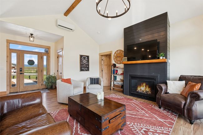 Living area featuring an inviting chandelier, a wall mounted AC, beam ceiling, wood finished floors, and high vaulted ceiling | Image 26