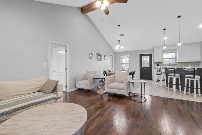 Living area featuring wood-type flooring, high vaulted ceiling, baseboards, beamed ceiling, and a ceiling fan | Image 4