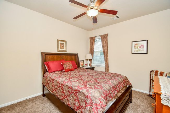 Bedroom with neutral walls and carpet, featuring a wooden bed frame with a red and gold patterned comforter. | Image 24