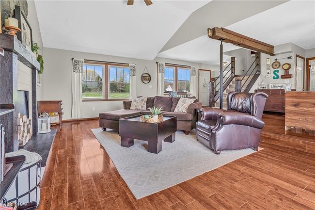 Living room featuring baseboards, vaulted ceiling, a fireplace, wood finished floors, and stairs | Image 11
