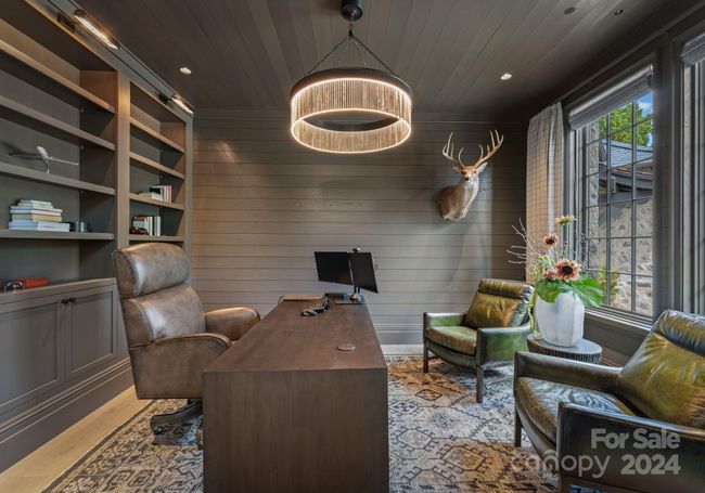 The study has custom built-in cabinetry and shelving with shiplap covered walls and ceilings with a one-of-a-kind chandelier as the focal point and library lighting for the perfect touch. | Image 8