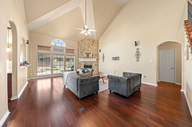 Living area featuring high vaulted ceiling, ceiling fan, a fireplace, arched walkways, and dark wood-style floors | Image 6