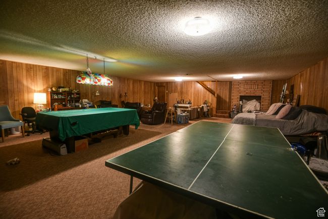 Playroom with wooden walls, billiards table, a textured ceiling, carpet flooring, and a fireplace | Image 32