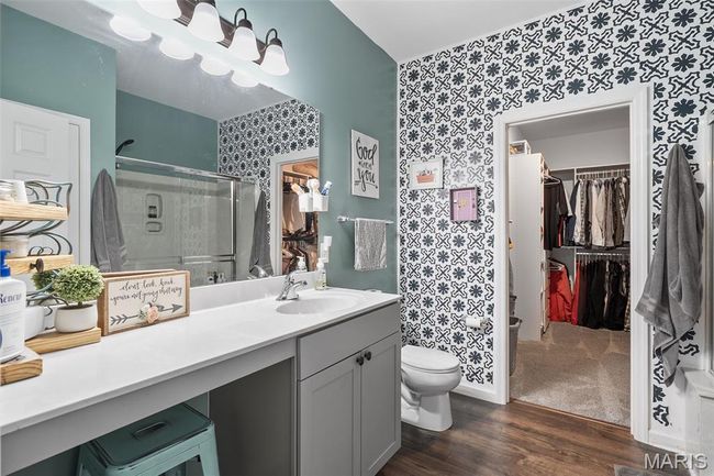 Bathroom featuring wallpapered walls, a spacious closet, wood finished floors, vanity, and a shower stall | Image 16