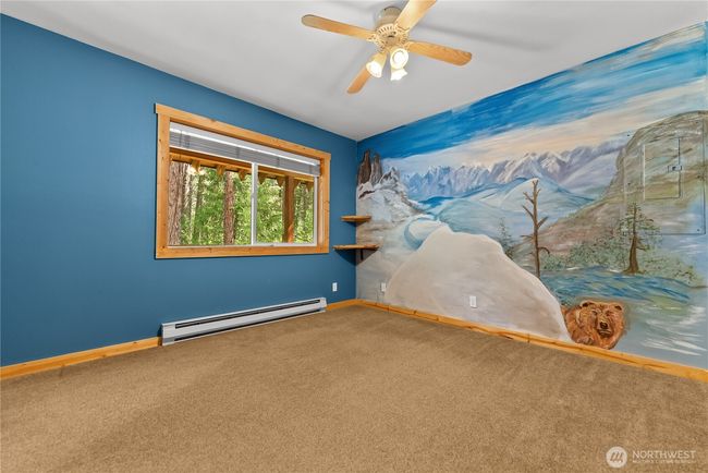 Main floor bedroom: Large window frames peaceful forested views and natural light Custom wall mural adds artistic flair with a scenic mountain landscape | Image 19