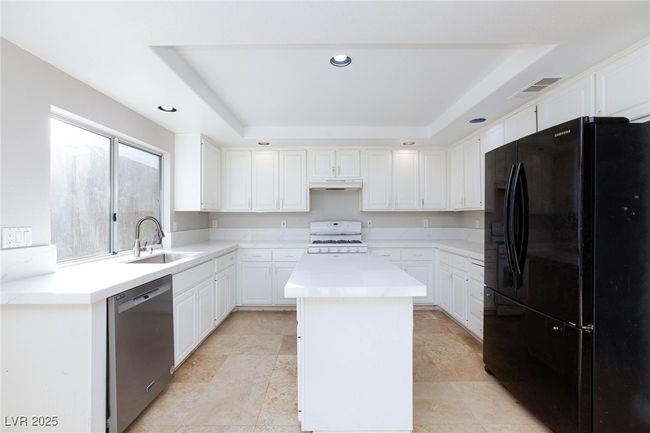 Kitchen with a raised ceiling, a sink, freestanding refrigerator, white range with gas cooktop, and stainless steel dishwasher | Image 14