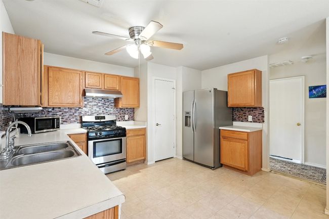 Kitchen featuring decorative backsplash, appliances with stainless steel finishes, light countertops, ceiling fan, and under cabinet range hood | Image 10