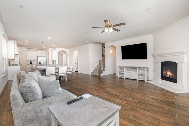 Living room featuring arched walkways, ceiling fan, a glass covered fireplace, and dark wood-style flooring | Image 5