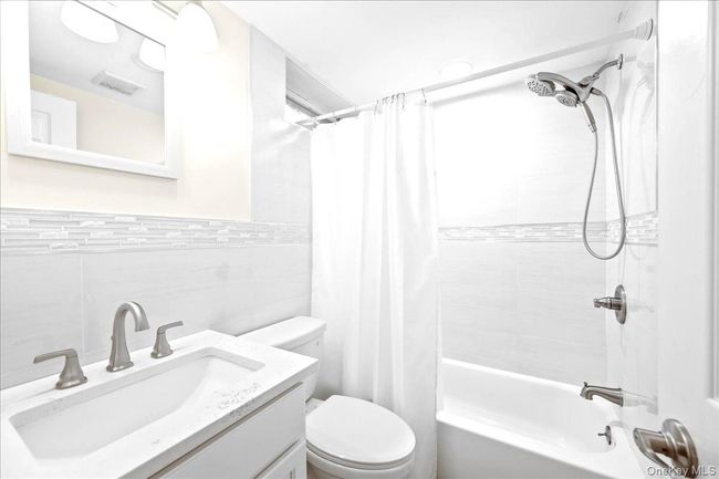 Bathroom with tile walls, toilet, shower / bathtub combination with curtain, and vanity | Image 33