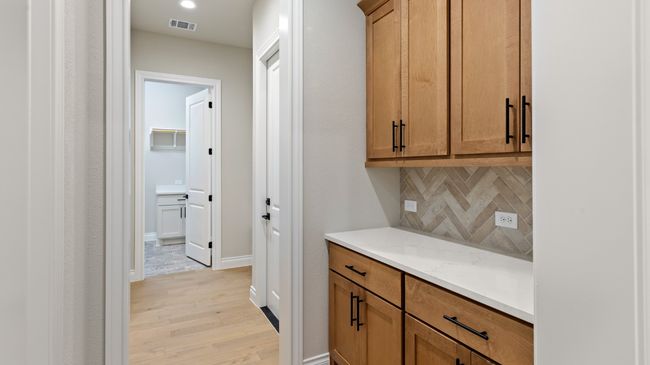 Bar area featuring brown cabinets, backsplash, light wood-style floors, and light stone countertops | Image 33