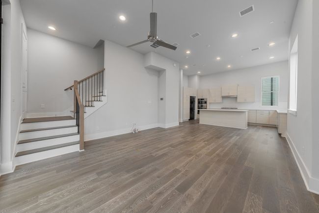 Unfurnished living room with stairs, a ceiling fan, wood finished floors, and visible vents | Image 12