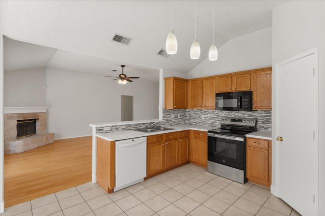 Kitchen with vaulted ceiling, light tile patterned floors, decorative backsplash, stainless steel electric stove, and dishwasher | Image 7