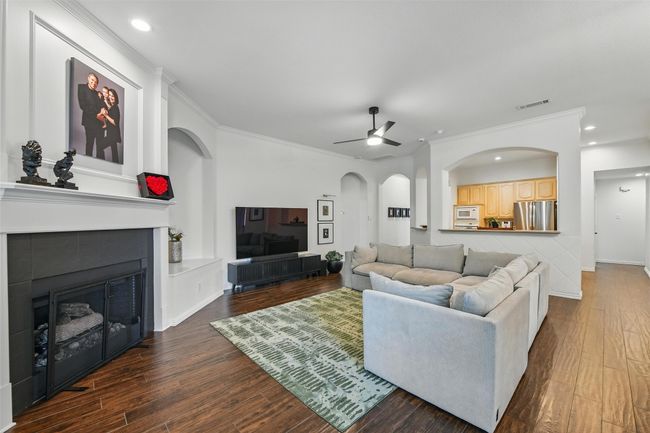 Living area featuring a ceiling fan, crown molding, wood finished floors, a tiled fireplace, and arched walkways | Image 14