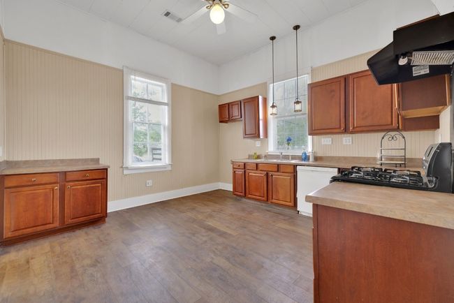 Kitchen with black gas range oven, under cabinet range hood, wood finished floors, white dishwasher, and ceiling fan | Image 12