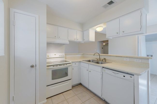 Kitchen with white appliances, a sink, under cabinet range hood, light tile patterned floors, and light countertops | Image 6