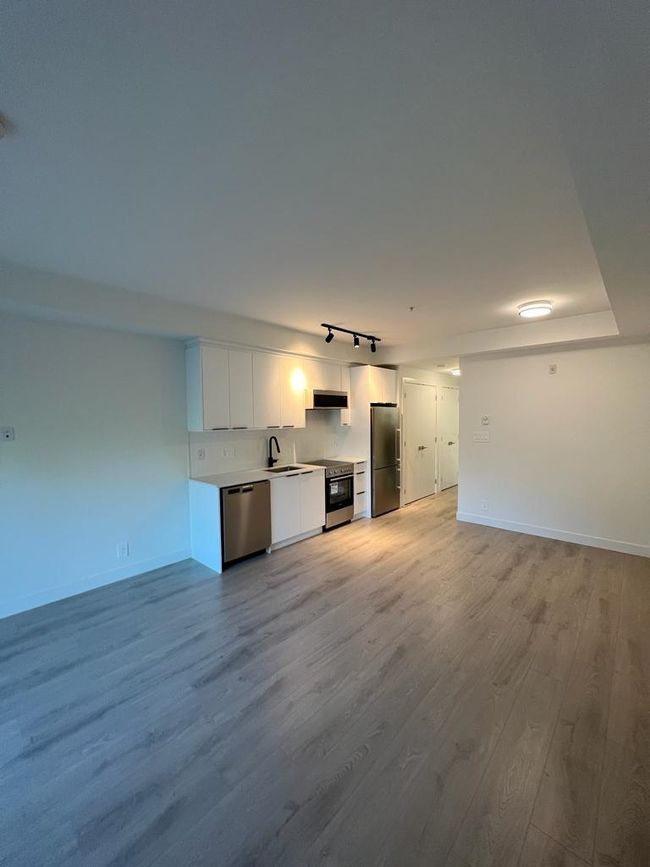 Unfurnished living room with baseboards, rail lighting, a sink, and light wood finished floors | Image 4