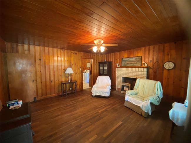 Living area featuring wood ceiling, a brick fireplace, wood finished floors, a ceiling fan, and wooden walls | Image 11