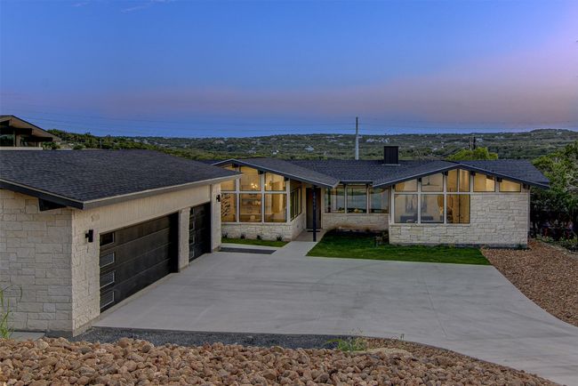 View of front of property with stone siding, a sunroom, a shingled roof, and a detached garage | Image 23
