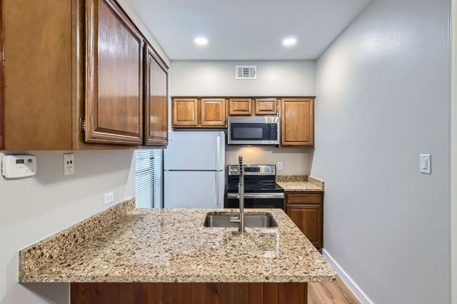 Kitchen with visible vents, appliances with stainless steel finishes, a peninsula, baseboards, and light stone countertops | Image 8