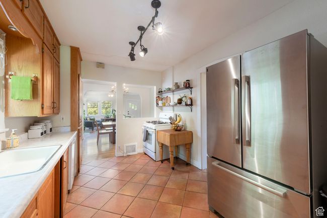 Kitchen with freestanding refrigerator, white gas range oven, light countertops, light tile patterned floors, and a chandelier | Image 13