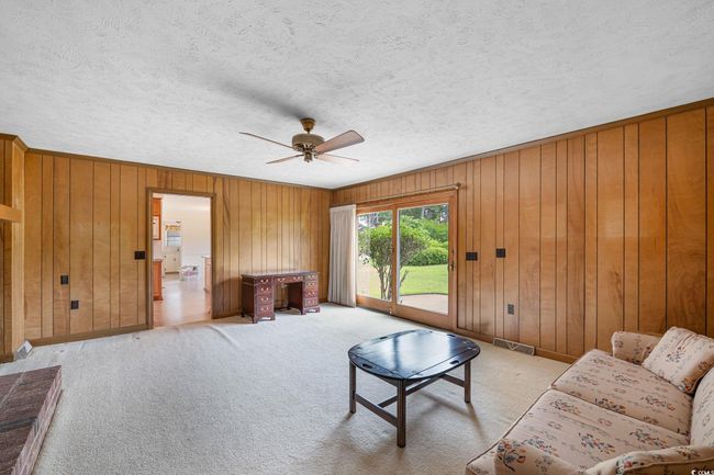 Living room featuring a ceiling fan, wooden walls, a textured ceiling, light carpet, and baseboards | Image 16