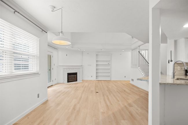 Unfurnished living room featuring a sink, light wood-type flooring, a tiled fireplace, and stairs | Image 6