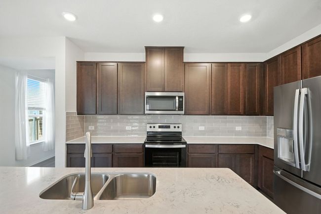 Kitchen featuring appliances with stainless steel finishes, decorative backsplash, light stone countertops, recessed lighting, and dark brown cabinetry | Image 11