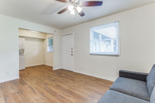 Living area featuring stacked washer and clothes dryer, light wood finished floors, baseboards, and ceiling fan | Image 4