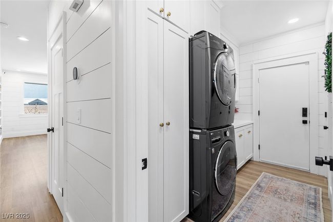 Clothes washing area featuring light wood-type flooring, stacked washing maching and dryer, recessed lighting, and cabinet space | Image 8