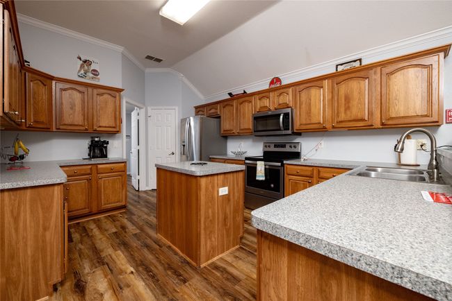 Kitchen featuring stainless steel appliances, vaulted ceiling, ornamental molding, a sink, and dark wood-style flooring | Image 16