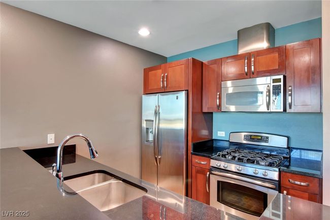 Kitchen with brown cabinets, dark stone countertops, stainless steel appliances, and a sink | Image 7