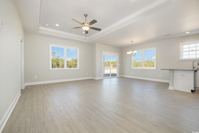 Unfurnished living room with ornamental molding, ceiling fan with notable chandelier, a tray ceiling, sink, and light hardwood / wood-style flooring | Image 9
