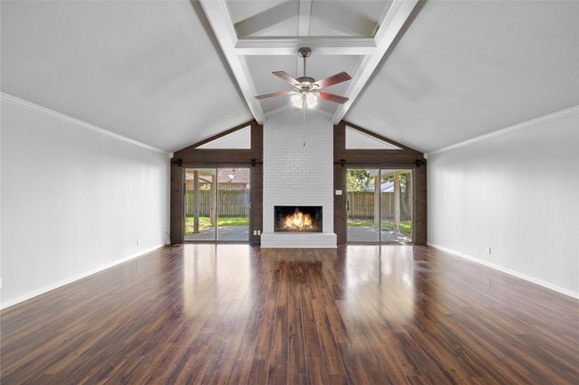 Unfurnished living room featuring wood finished floors, a brick fireplace, baseboards, and plenty of natural light | Image 4