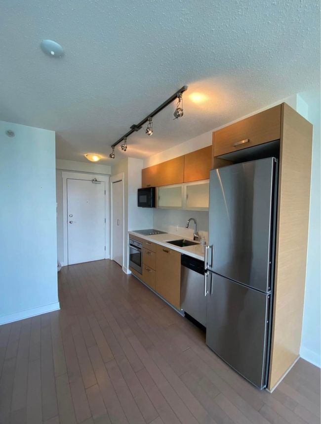 Kitchen with a textured ceiling, a sink, light countertops, black appliances, and wood finished floors | Image 11