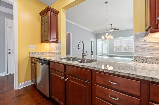 Kitchen featuring dark wood finished floors, stainless steel dishwasher, decorative backsplash, and a sink | Image 10