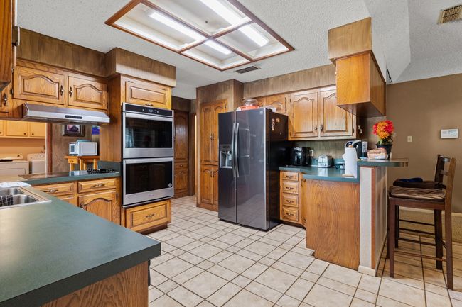 Kitchen with washing machine and clothes dryer, a kitchen breakfast bar, stainless steel appliances, a peninsula, and visible vents | Image 21