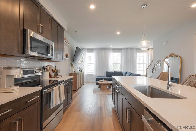 Kitchen with stainless steel appliances, a sink, dark brown cabinets, open floor plan, and light countertops | Image 13