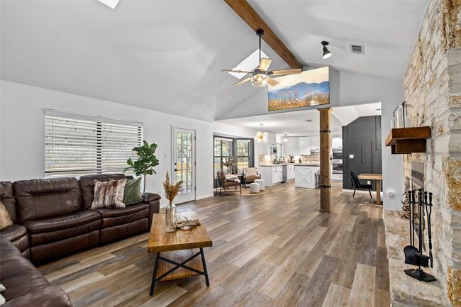 Living room featuring a stone fireplace, a ceiling fan, wood finished floors, beamed ceiling, and high vaulted ceiling | Image 8