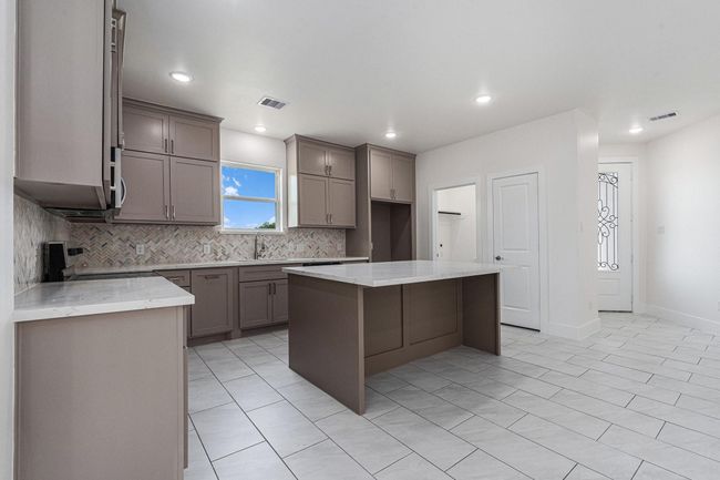 This spacious kitchen features modern cabinetry, a large central island, and sleek tile flooring. The neutral tone palette and ample natural light create a bright and inviting space, perfect for cooking and entertaining. | Image 12