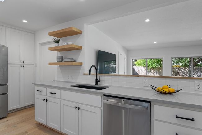 The kitchen stuns with quartz counters and oak accents that echo the floors and floating shelves | Image 12